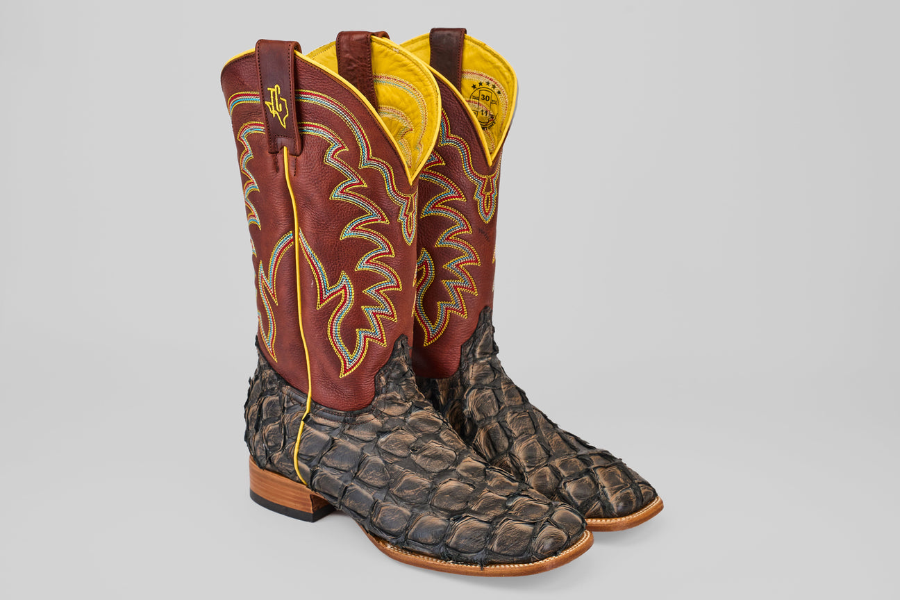 A pair of cowboy boots with brown suede foot and bright blue shaft, featuring intricate white and orange stitching, displayed side by side on a neutral background.