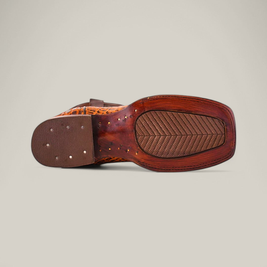 The image displays the sole of the Alligatoar Horn Back Print Honey - Square Toe shoe, a brown leather piece with textured and smooth elements. Metal studs on the heel, an alligator horn back print, and a patterned tread design enhance its exotic appeal.