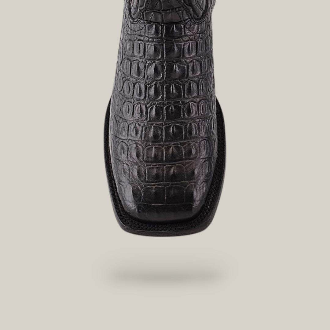 A close-up of the Alligatoar Horn Back Print Black boot showcases exquisite craftsmanship and a crocodile skin pattern on the upper. The square toe design adds modern flair against a light beige background.