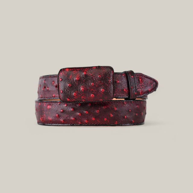 The Ostrich Print Black Cherry Belt features a rich red color with a dimpled texture and a plain light background. It combines elegance with rugged style through its square cowboy buckle and stitched details.