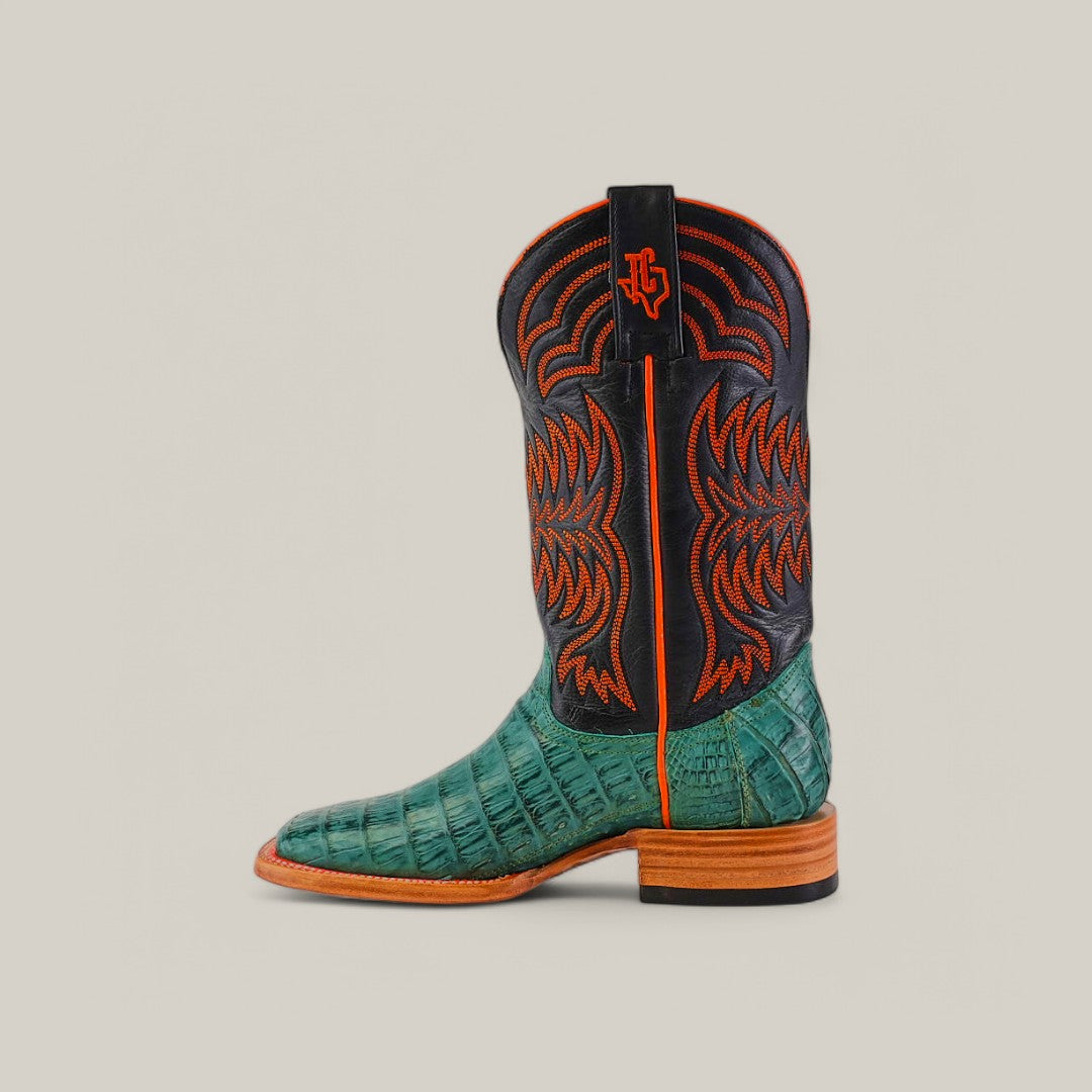 The Exotic Caiman Belly Tail - Green boot features premium caiman leather with an alligator texture, a black shaft with orange stitching and logo, a wooden heel, and pull-tab, all set against a plain light gray background.