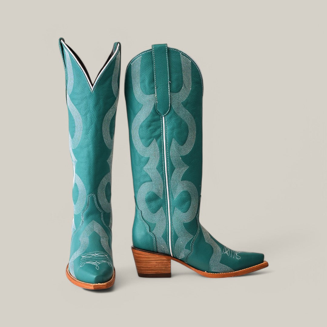A pair of Olimpia Green Teel cowboy boots features intricate white stitching and patterns. One boot faces forward, while the angled snip-toe design showcases the premium materials and stacked wooden heel, all set against a plain neutral background.