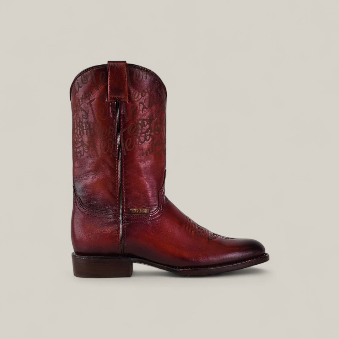 The Wyatt - Cogñac - Roper Toe is a single red leather cowboy boot with decorative stitching, a low heel, and pull strap, shown in side profile against a plain beige background.