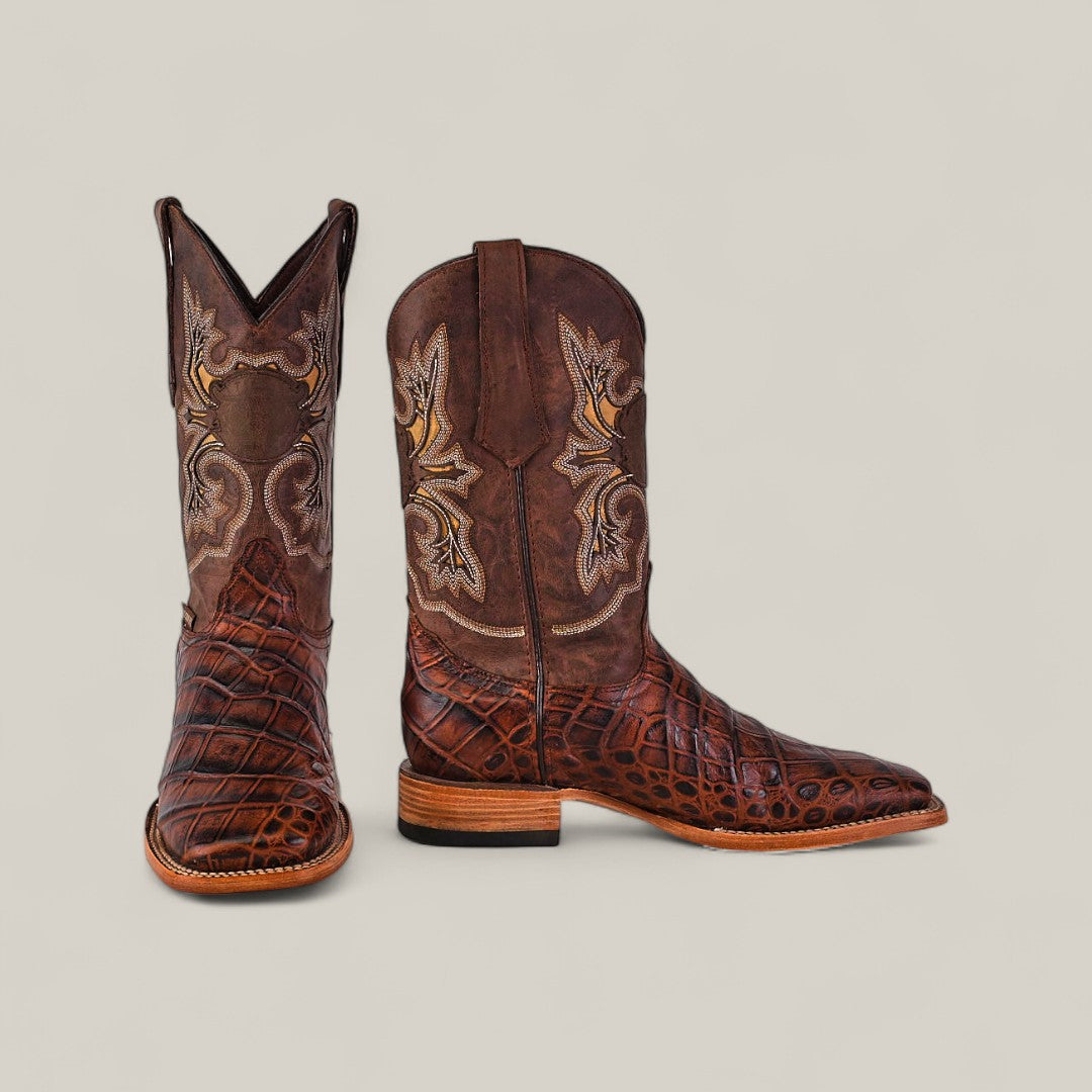 The Jonh - Brown - Square Toe boots feature premium leather, intricate stitching, and a textured reptile-like pattern on the lower section. Set on a plain light background, one boot stands upright while the other lies sideways.