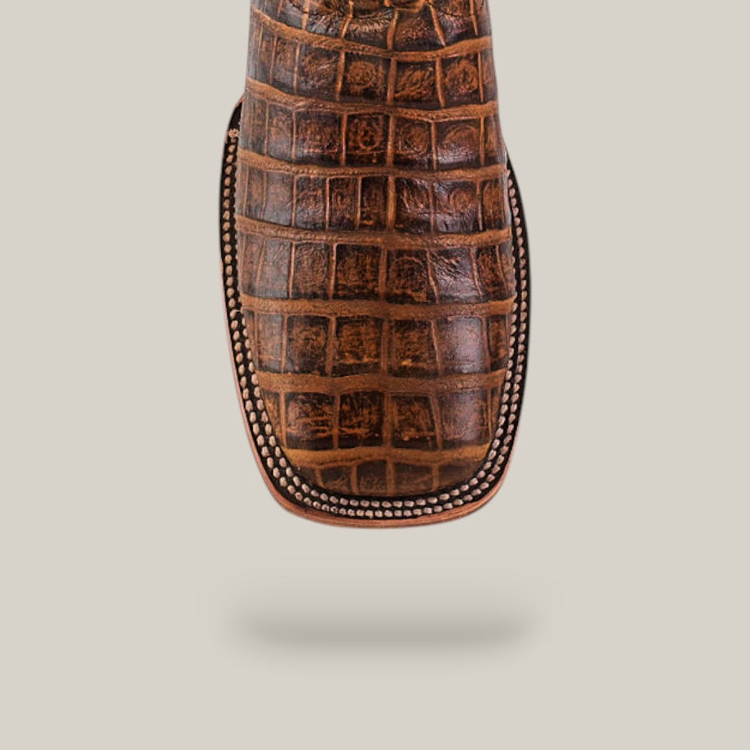 Close-up of the Ross - Orix - Square Toe cowboy boot’s brown, crocodile-patterned toe with detailed stitching, highlighting its quality craftsmanship against a plain beige background.