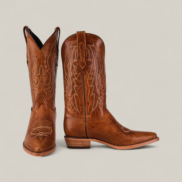 The Fresno - Fawn - Snip Toe cowboy boots, crafted from premium leather with decorative stitching, are shown on a plain light background—one standing upright, the other leaning against it.