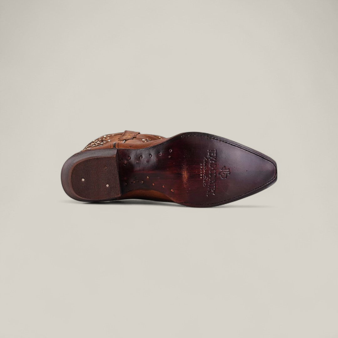 The Dolly - Brown - Snip Toe boot is shown from the bottom, featuring a pointed snip toe, decorative stitching, wooden heel, and visible makerâs logo on the sole against a plain light background.