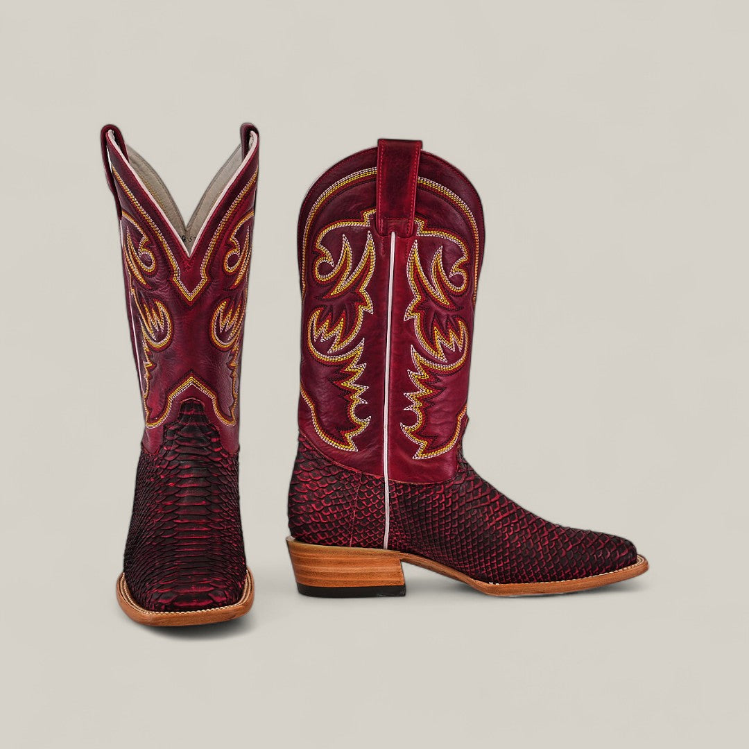 A pair of Exotic Python - Cherry Nobuck Square Toe boots with intricate yellow and white stitching, textured leather foot, and tan wooden heels, displayed on a light beige background.