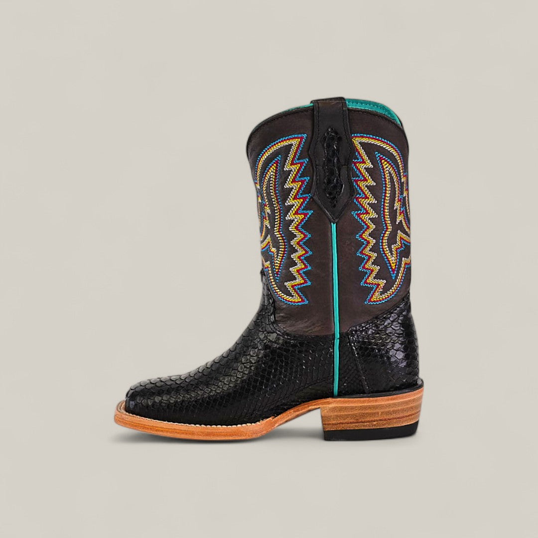 The Exotic Python Black - Square Toe - Kids Boots feature a textured, snakeskin-like surface, colorful zigzag stitching in yellow, orange, and blue on the shaft, and a light brown wooden heel against a beige background.