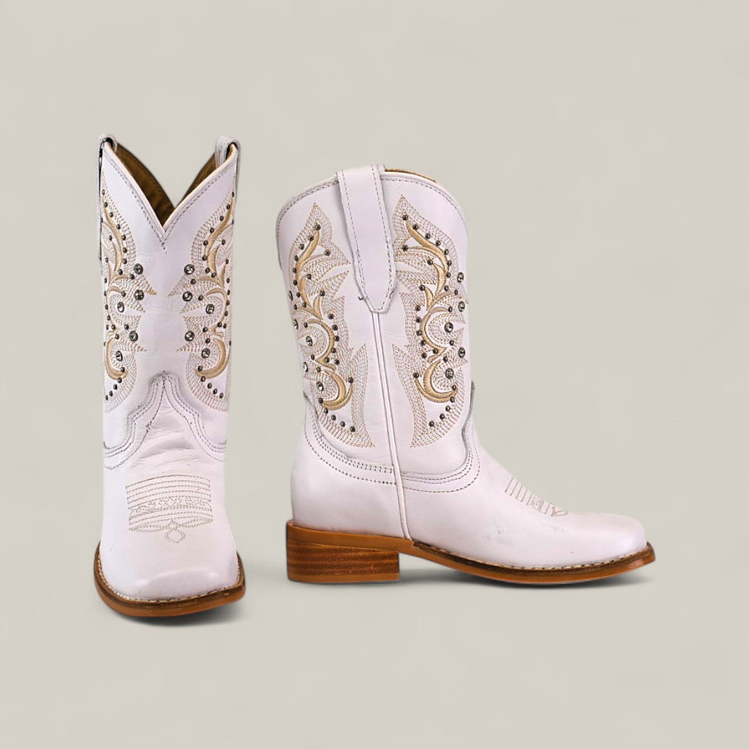 The Amara White - Square Toe - Kids Boots feature light pink leather, intricate tan and white stitching, decorative cutouts, and medium wooden heels for stylish comfort, displayed against a plain beige background.