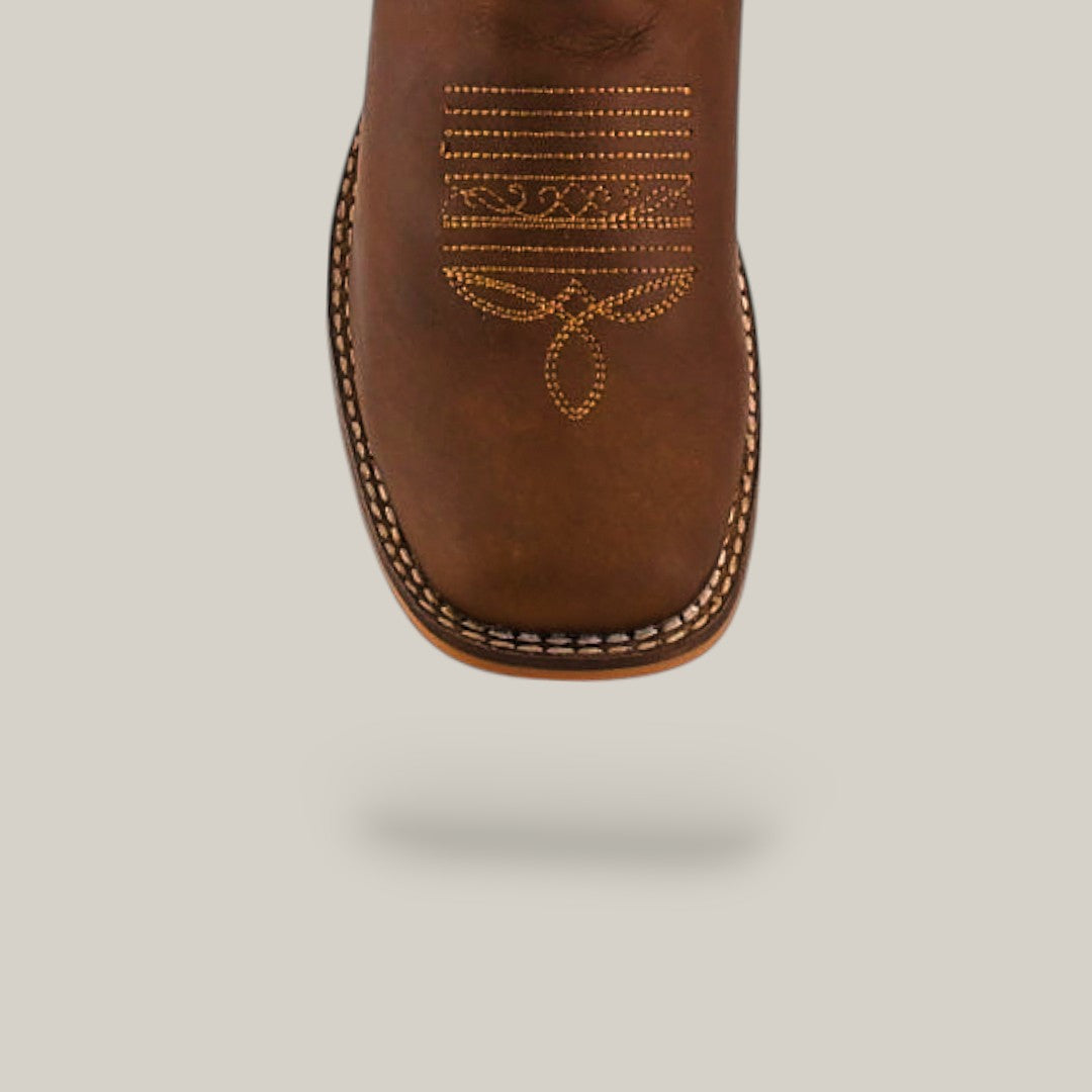 Close-up of the toe on the Premiere Texas Copper - Square Toe - Kids Boots, featuring brown leather with decorative yellow and white stitching for classic Texas style, set against a light beige background.