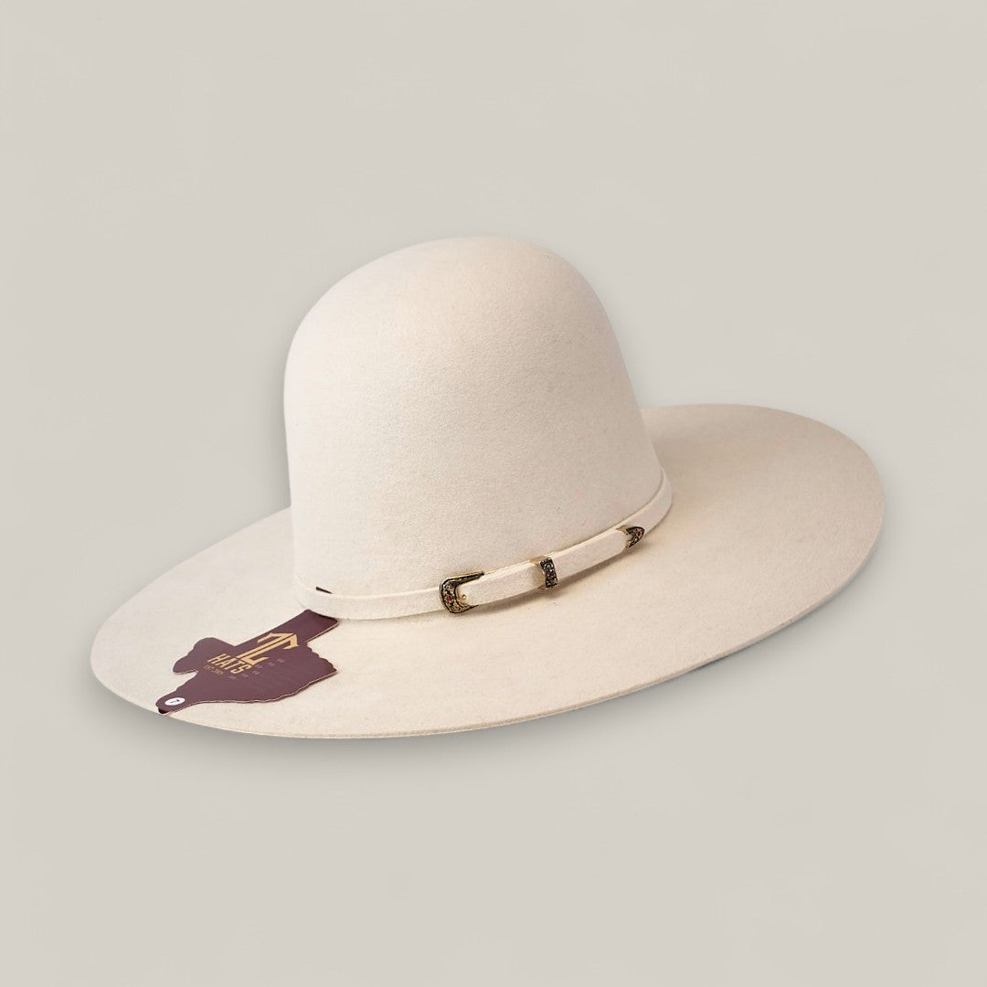 The 10x White - TC Hats is a wide-brimmed, off-white felt Western hat featuring a rounded open crown, a decorative braided band, and a brown tag hanging from the brim, shown against a plain light background.
