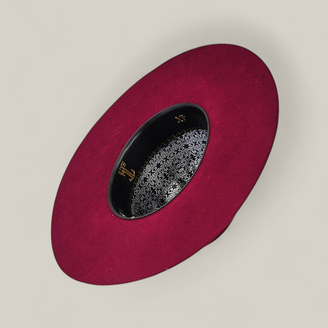 The 4X Burgundy - TC Hats is displayed from above, showcasing its wide maroon brim, open crown, decorative black inner band, and intricate silver-and-black patterned lining. The background is a simple light beige.
