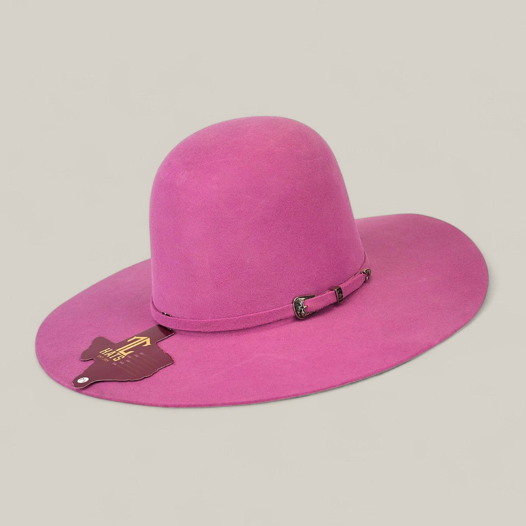 The 4x Pink - TC Hats is a bright pink, wide-brimmed Western hat in texana style with an open crown, a decorative band with silver buckle and brown tag, shown against a plain light beige background.