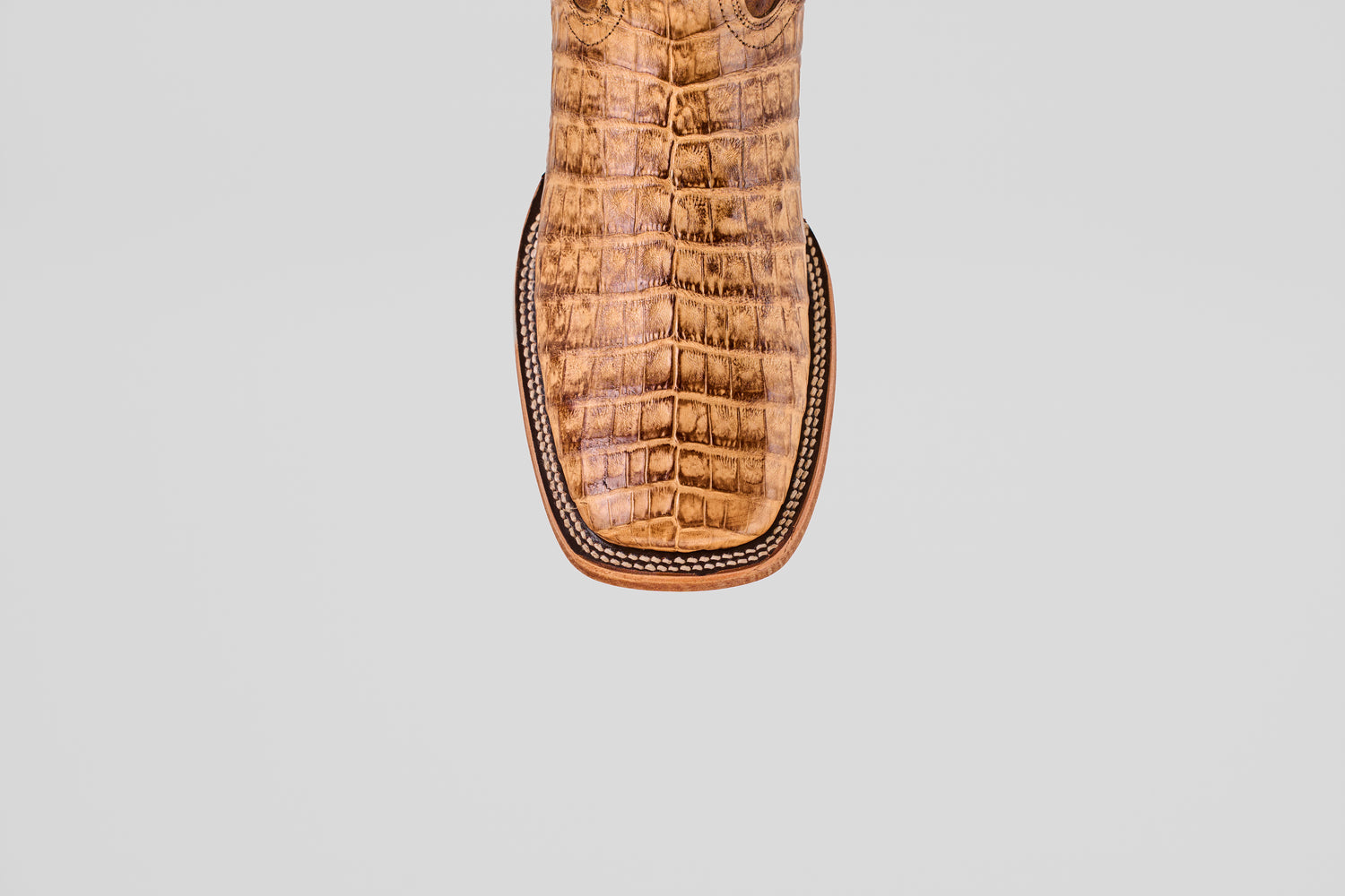 Close-up of the Exotic Caiman Belly - Antique - Square Toe boot’s toe, showcasing textured caiman leather with a crocodile pattern and detailed edge stitching, set against a light gray background.
