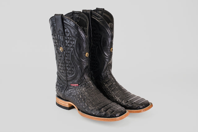 The Exotic Caiman Horn Back - Black - Square Toe boots feature black textured caiman leather with a crocodile pattern, tan leather soles, and decorative stitching, displayed on a light gray background.