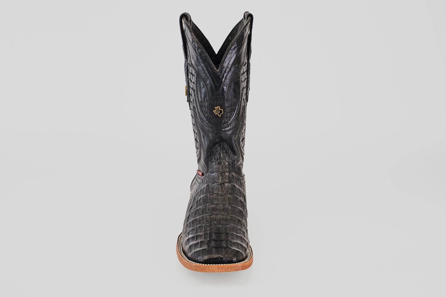 A single Exotic Caiman Horn Back boot in black with a square toe, tan sole, and decorative stitching, photographed from the front against a plain white background.