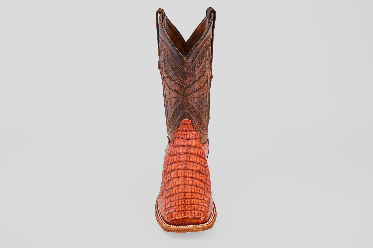 The Exotic Caiman Horn Back - Brandy - Square Toe boot, featuring a brown textured shaft and reddish patterned foot, is displayed facing forward on a plain light gray background.
