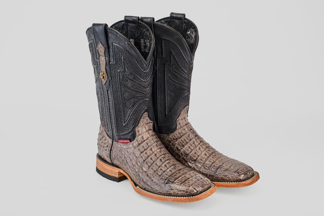 The Exotic Caiman Horn Back - Serpentine - Square Toe boots feature textured brown caiman leather, black shafts with intricate stitching, and wooden soles, displayed on a plain light gray background.