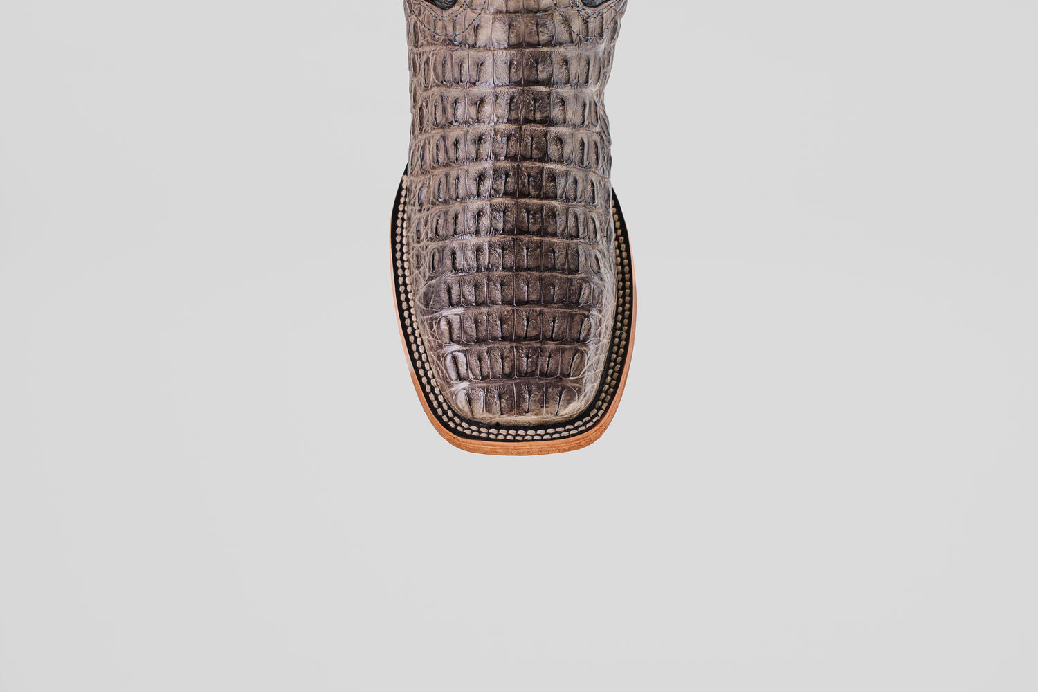 A close-up of the Exotic Caiman Horn Back - Serpentine - Square Toe boot’s brown, crocodile-embossed leather toe with detailed edge stitching, shown against a plain white background.