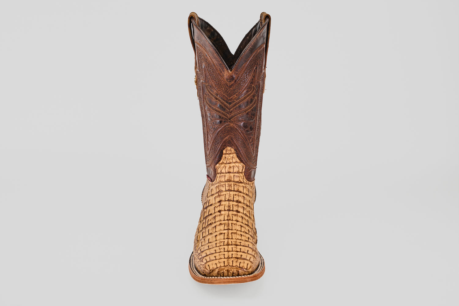 The Exotic Caiman Horn Back - Antique - Square Toe boot features a textured light tan lower and a dark brown, ornately stitched upper section, displayed front-facing on a plain light gray background.