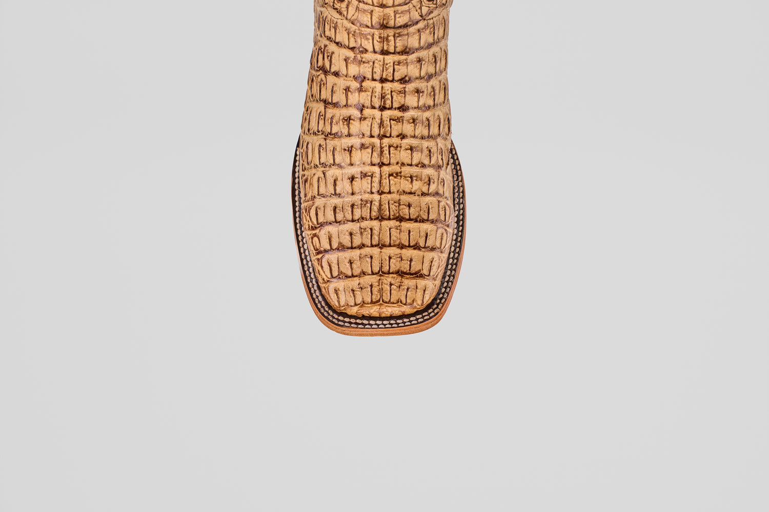 A close-up of the toe of the Exotic Caiman Horn Back - Antique - Square Toe boot, featuring a striking crocodile pattern in tan, set against a plain light gray background.