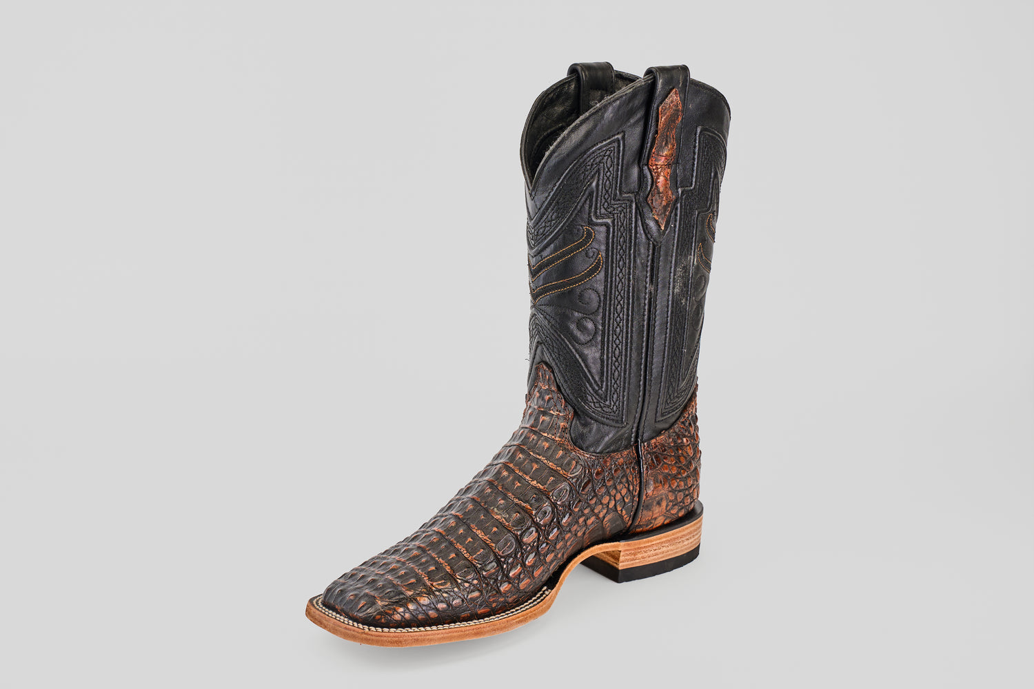 The Exotic Caiman Horn Back - Roma - Square Toe boot features a brown textured caiman leather foot and a tall black intricately stitched shaft, displayed against a plain light gray background.
