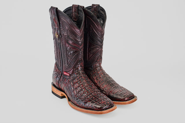 A pair of Exotic Caiman Horn Back boots in Black Cherry with a square toe and light brown soles, featuring an intricate reptile-like texture, displayed against a plain light gray background.