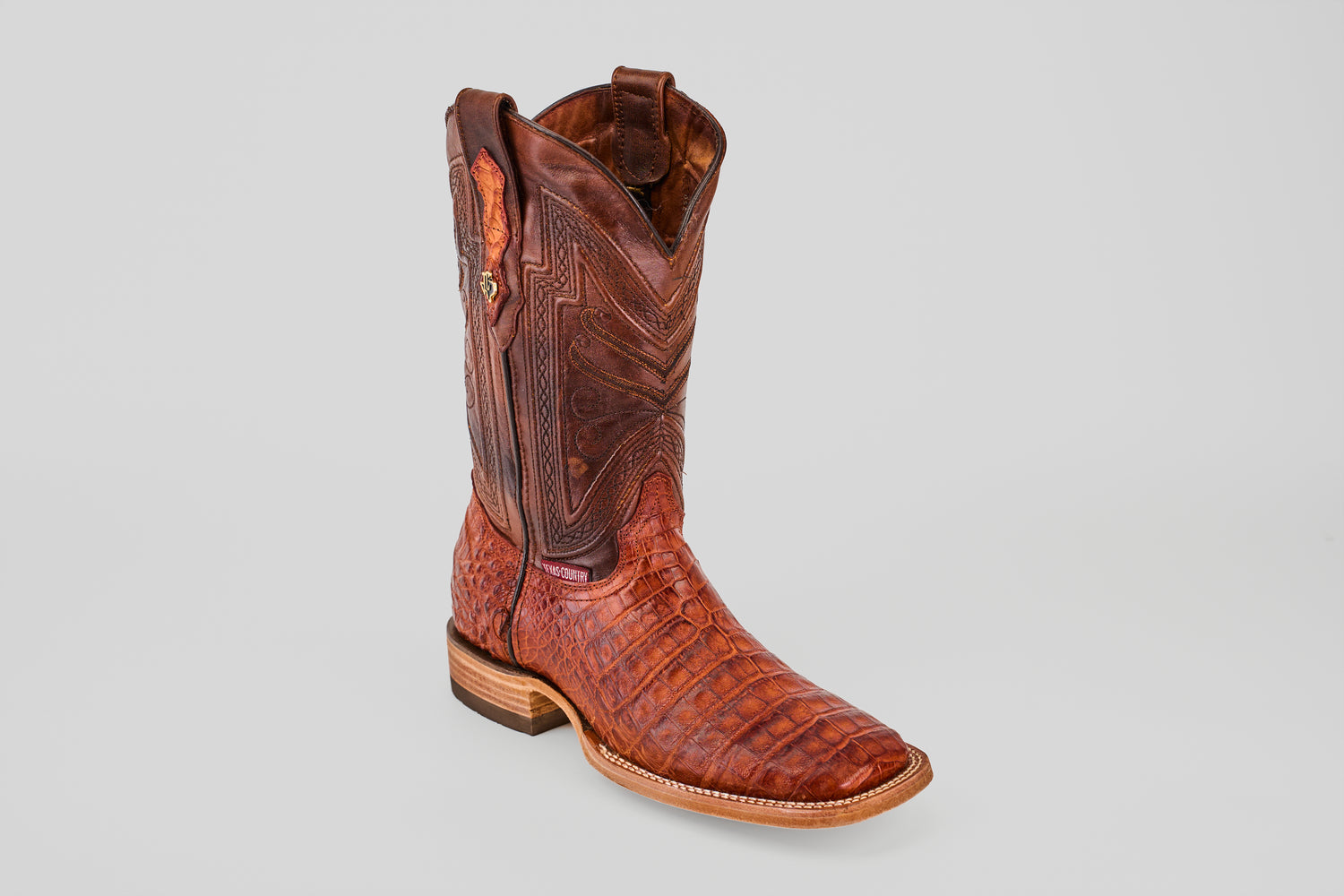 The Exotic Caiman Belly - Brandy - Square Toe boot features a rich brown hue, textured crocodile-like pattern, and decorative stitching, highlighting its luxurious exotic leather against a plain light gray background.