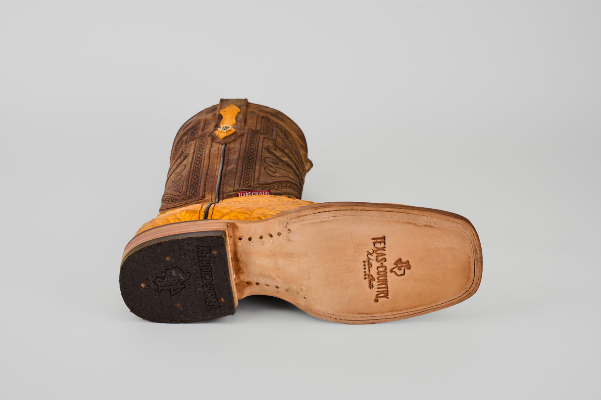 A single Exotic Caiman Horn Back - Buttercup Square Toe boot lies on its side, revealing the tan finish, detailed stitching, intricate upper design, stamped sole, and a black rubber heel.