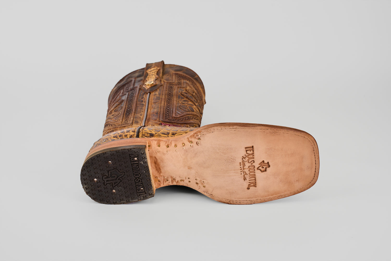 A single Exotic Caiman Horn Back - Biza Camel - Square Toe boot lies on its side, displaying the detailed sole with LUCCHESE and logo stamped on light tan leather, set against a plain white background.