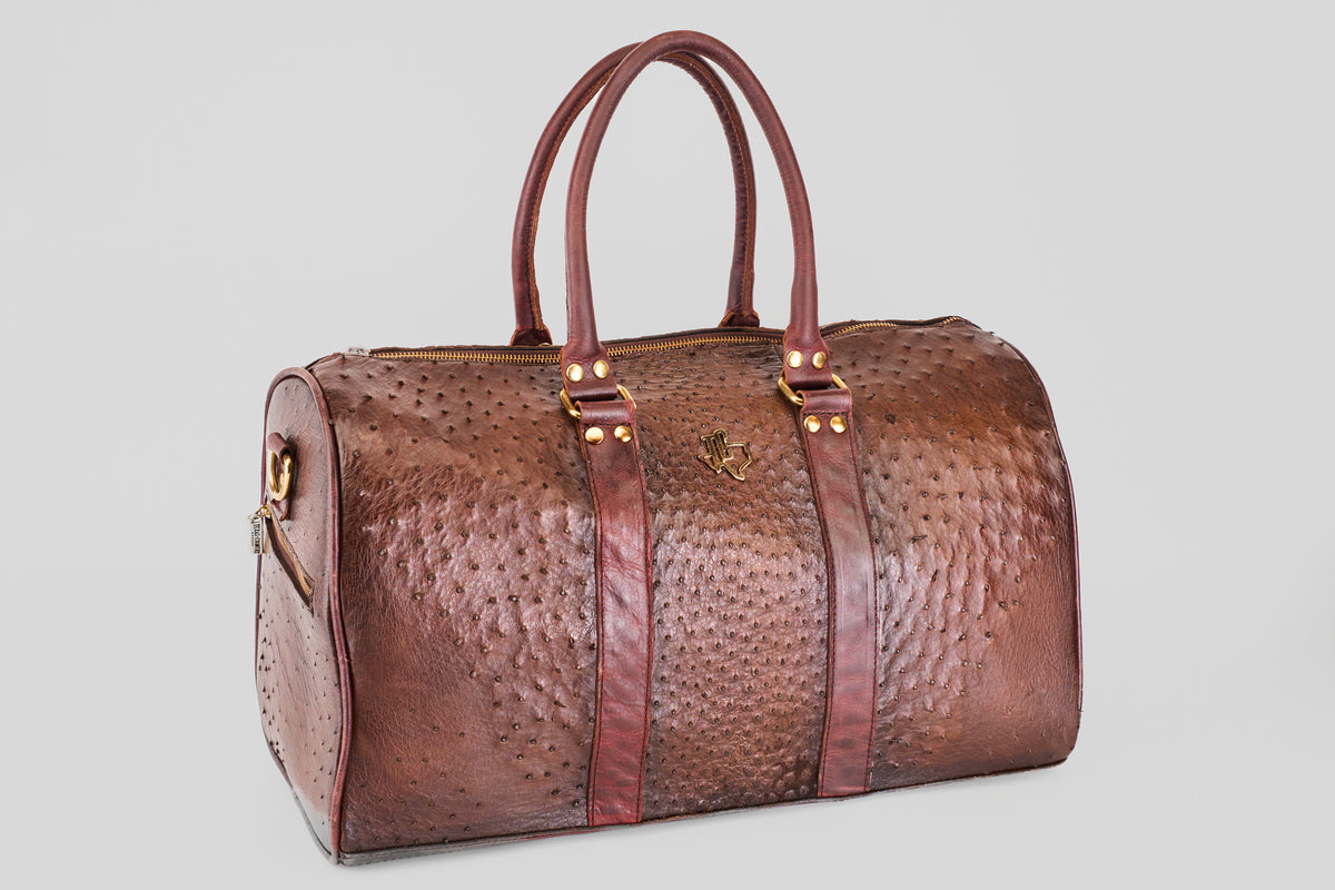 The Exotic Full Quilt Ostrich - Brown - Travel Bag, featuring two handles, gold hardware, and vertical straps, is a luxurious companion for chic travelers and is shown resting on a plain light gray background.