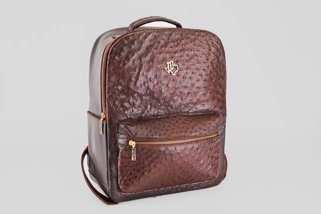 The Exotic Full Quilt Ostrich - Brown - BackPack features a textured, dimpled surface, gold zippers, and a gold emblem on the front pocket—an ideal luxurious travel companion shown on a plain light gray background.