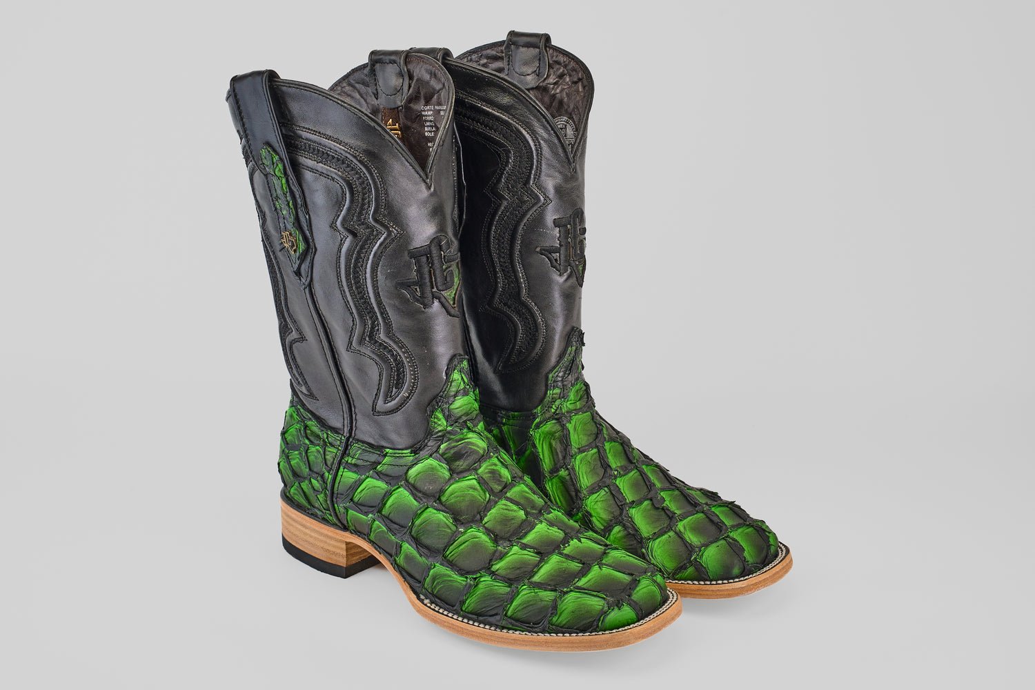 The Conor - Swamp Green - Square Toe boots feature black leather uppers, bright green scale-patterned lowers inspired by Pirarucu fish, and light tan soles and heels, shown on a light gray background.