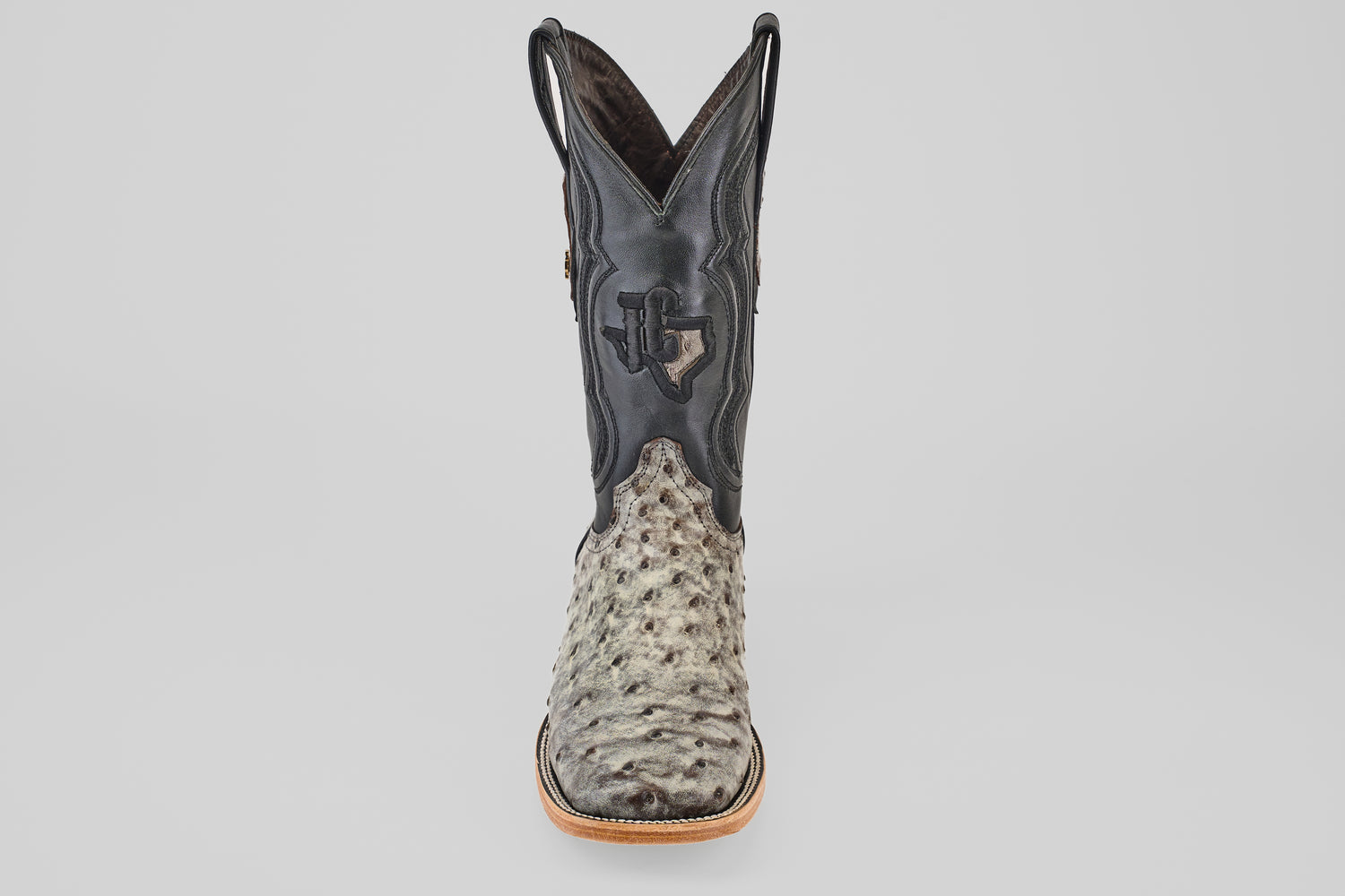 A single mens Exotic Full Quilt Ostrich - Nicotine - Square Toe boot with a textured light gray and black leather foot, black leather upper, decorative stitching, and Texas emblem, shown on a plain white background.