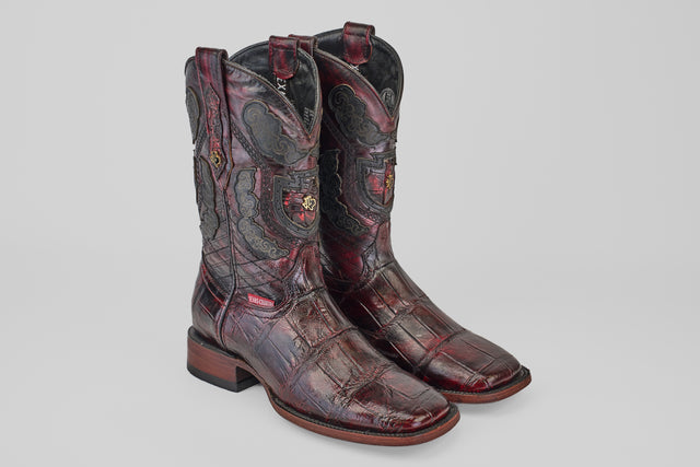The Exotic Alligator - BlackCherry Square Toe boots feature dark red textured alligator leather, black and gray decorative stitching, crest designs on the shafts, and low wooden heels against a plain light background.