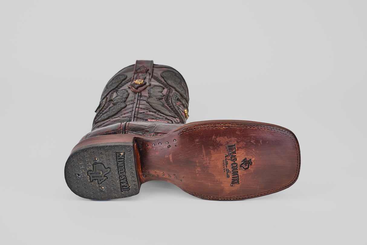 A single Exotic Alligator - BlackCherry - Square Toe boot rests on its side, revealing a HANDCRAFTED-stamped leather sole with a horse logo. The brown boot showcases decorative stitching, a black rubber heel, and alligator-quality craftsmanship.