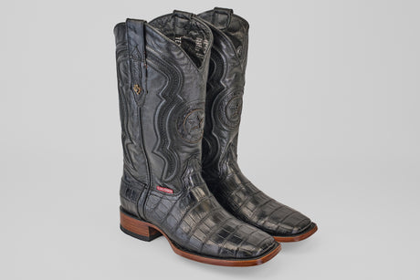 A pair of Exotic Alligator Tail - Black - Square Toe boots, featuring embossed leather, wooden soles, and detailed shaft stitching, displayed on a plain light gray background.