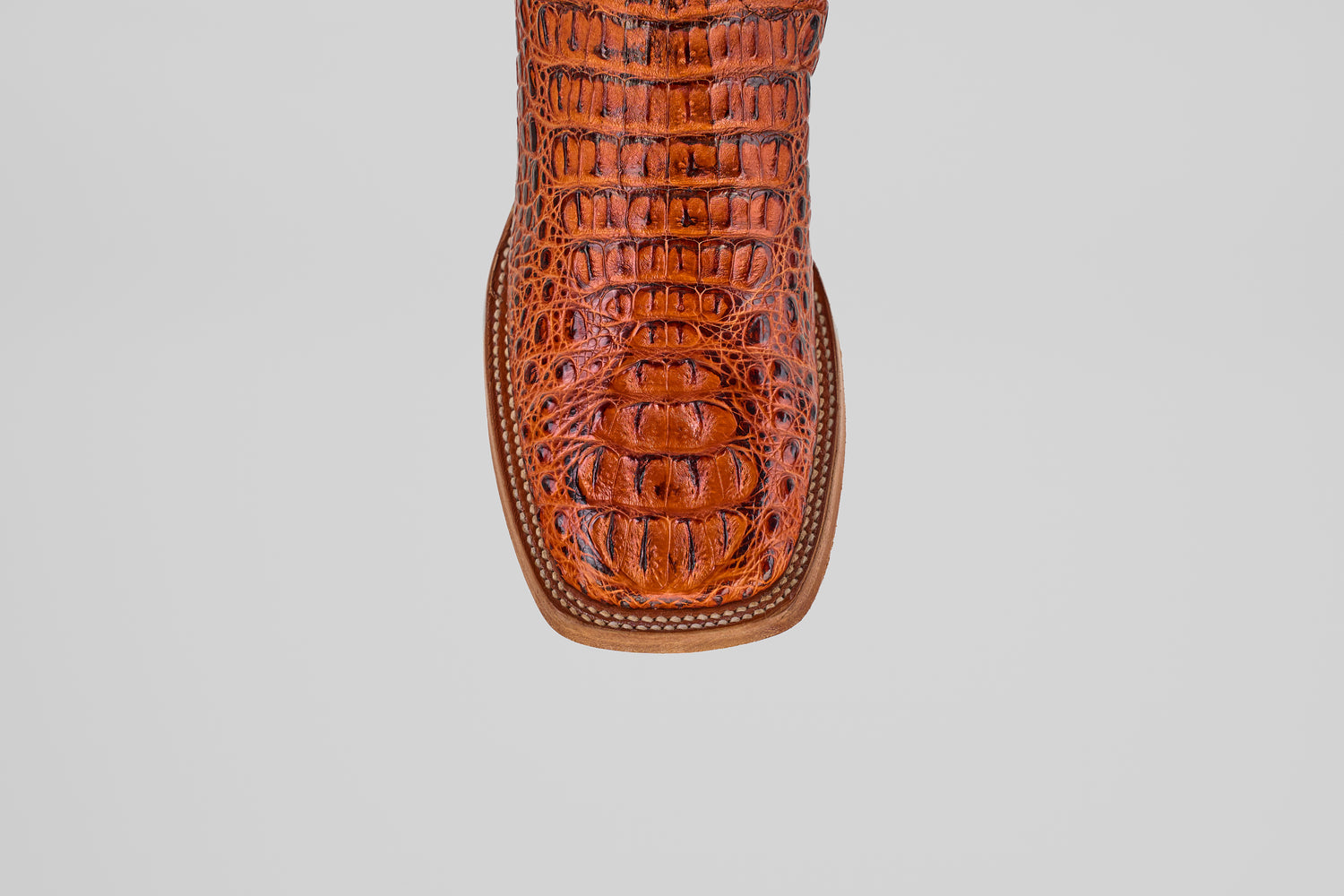 A top-down close-up of the Exotic Caiman Head - Cogñac - Square Toe boot, featuring rich brown caiman leather with a textured crocodile pattern, set against a plain gray background.