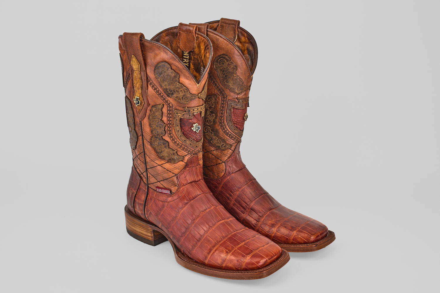 The Exotic Alligator Tail - Brick - Square Toe boots feature genuine reddish-brown alligator leather with intricate stitching and decorative shaft patterns, showcased against a plain light gray background.