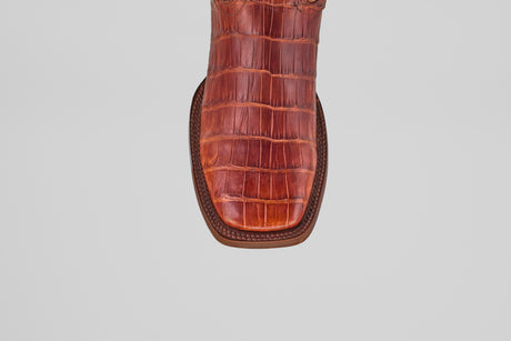 A close-up, top-down view of the Exotic Alligator Tail - Brick - Square Toe boot’s reddish-brown, square toe with genuine alligator leather texture, displayed against a plain light gray background.