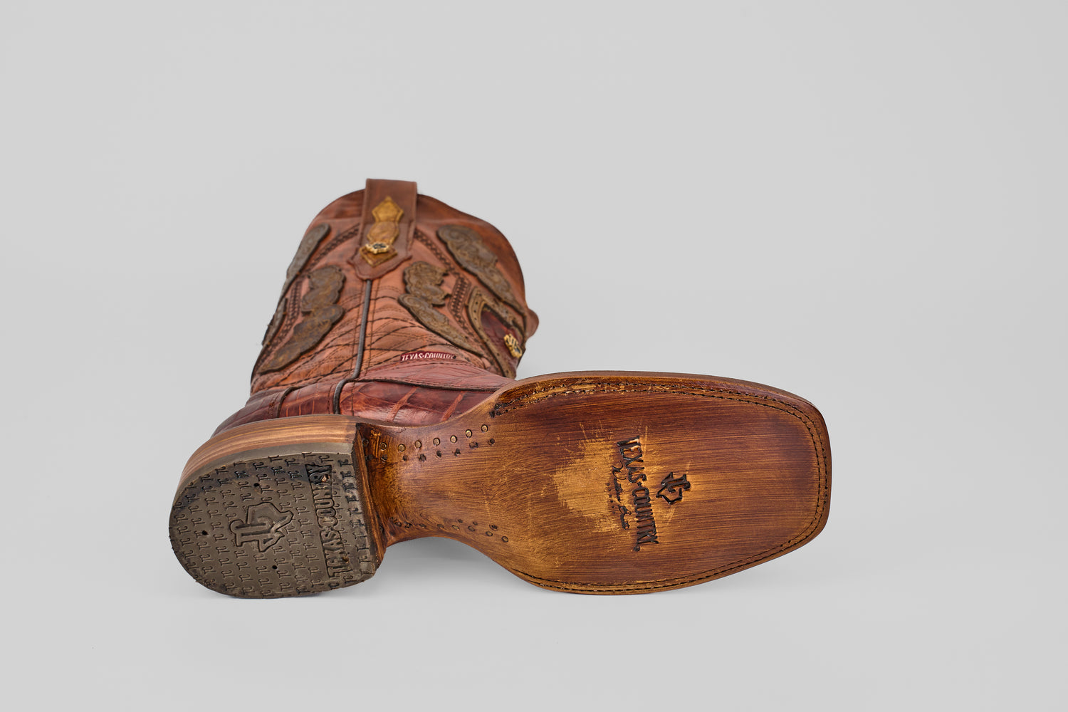 A single Exotic Alligator Tail - Brick - Square Toe cowboy boot lies on its side with the sole and heel stitching details and branding mark visible against a plain light gray background.