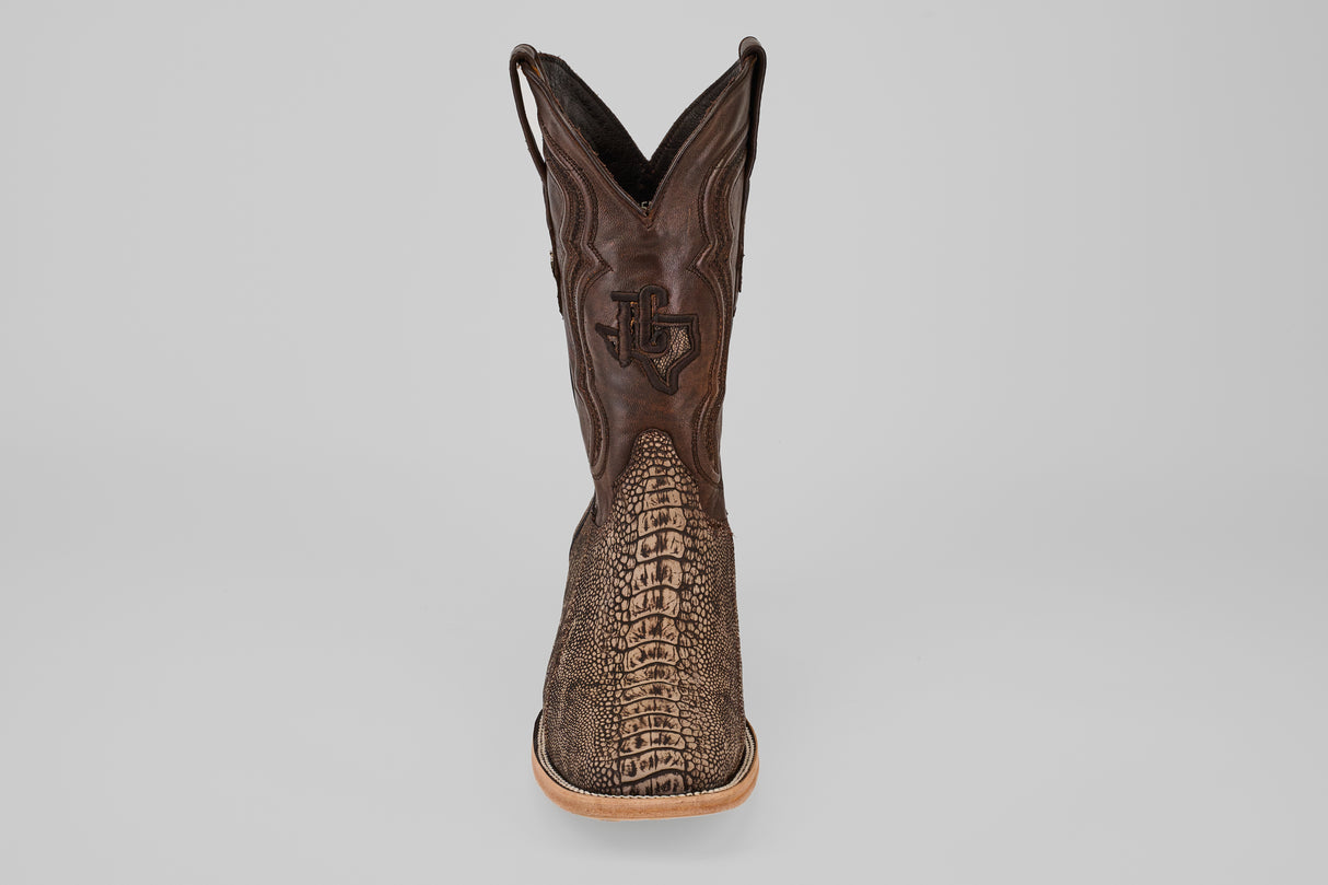 A single Exotic Full Quilt Ostrich Leg - Matte Orix - Square Toe boot, featuring a textured brown patterned front, light tan sole, and decorative shaft stitching, displayed upright on a plain gray background.