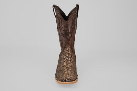 A single Exotic Full Quilt Ostrich Leg - Matte Orix - Square Toe boot, featuring a textured brown patterned front, light tan sole, and decorative shaft stitching, displayed upright on a plain gray background.