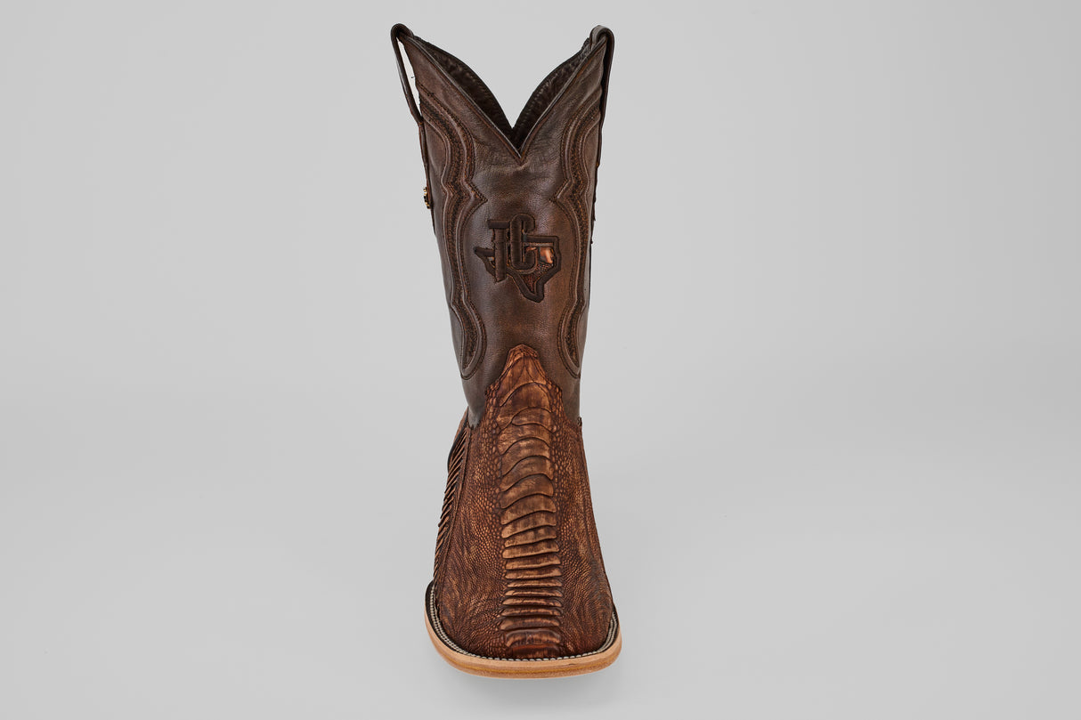 A single Exotic Full Quilt Ostrich Leg boot in Rustic Brick with a square toe, featuring intricate stitching and textured patterns, seen from the front against a plain gray background.