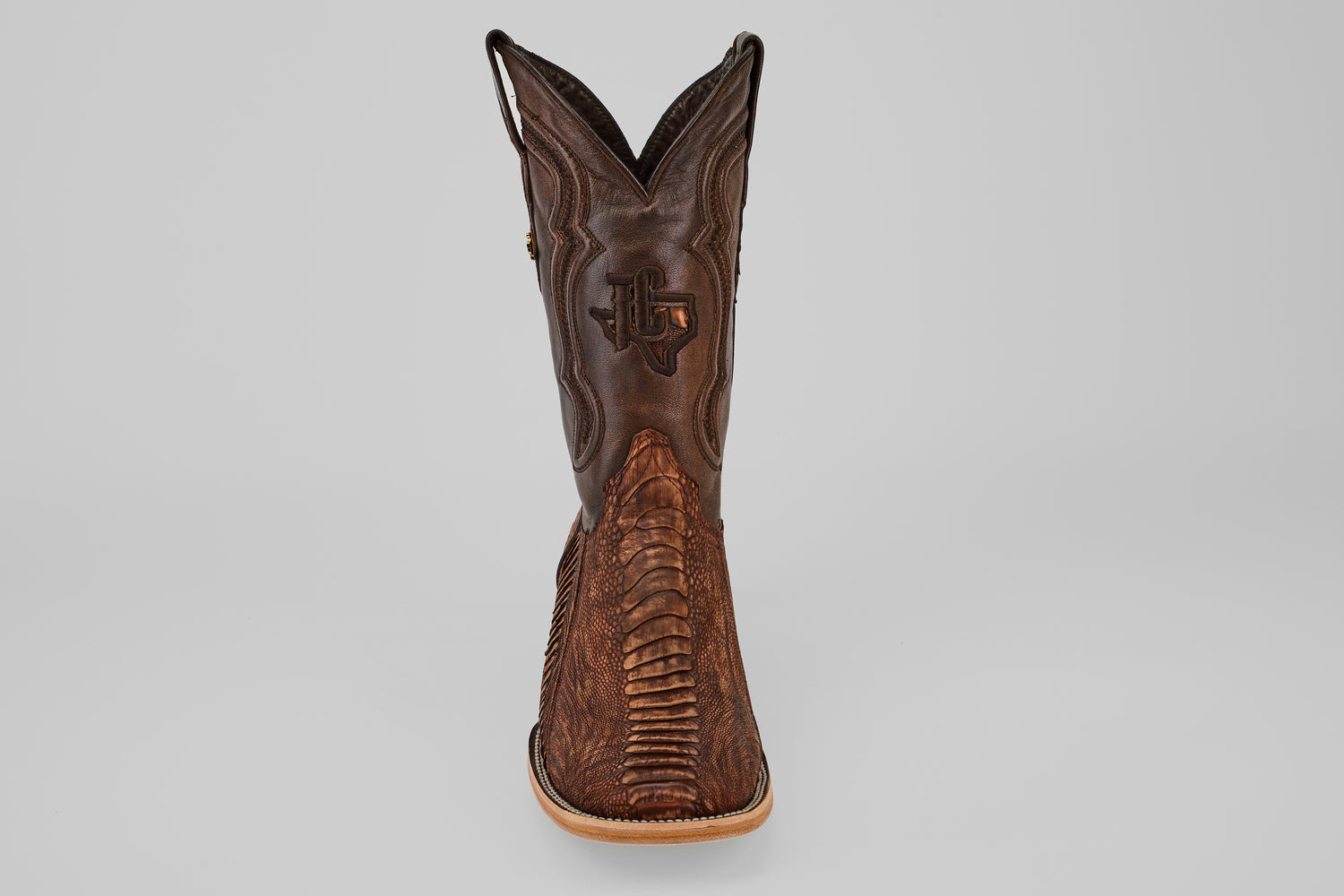 A single Exotic Full Quilt Ostrich Leg boot in Rustic Brick with a square toe, featuring intricate stitching and textured patterns, seen from the front against a plain gray background.