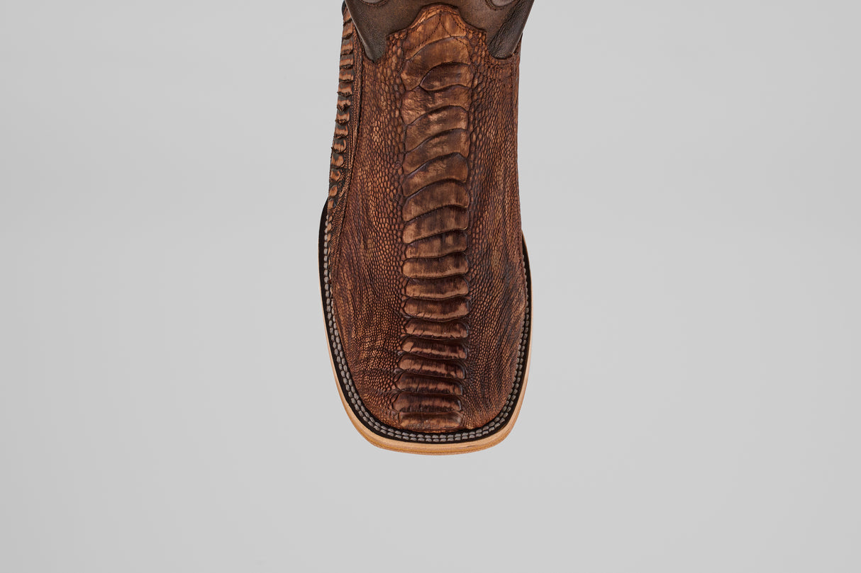 Close-up top view of the Exotic Full Quilt Ostrich Leg - Rustic Brick, a square-toed cowboy boot in brown with textured, patterned ostrich leg leather and detailed edge stitching. Set against a plain light gray background.