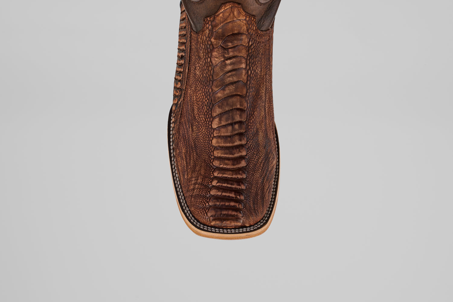 Close-up top view of the Exotic Full Quilt Ostrich Leg - Rustic Brick, a square-toed cowboy boot in brown with textured, patterned ostrich leg leather and detailed edge stitching. Set against a plain light gray background.