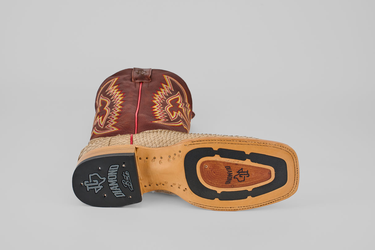 The Braxton - Cappucino - Square Toe mens boot features a tan sole and heel, a black Diamond logo on the sole, decorative stitching, and a brown leather upper. It lies on its side showcasing its luxury craftsmanship.