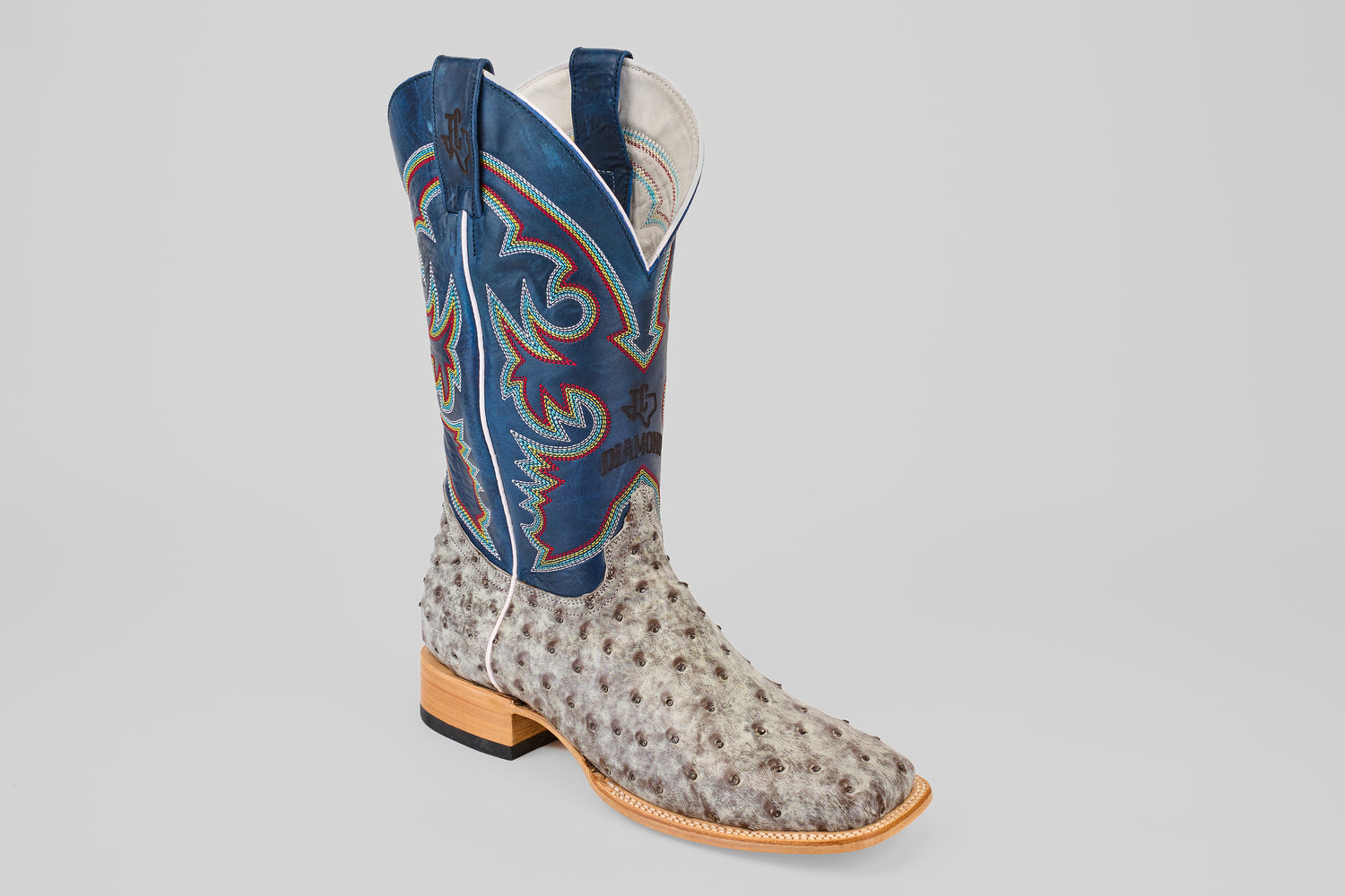 The Russell - Rustic Gray - Square Toe boot features textured light gray ostrich leather, a tall blue shaft with colorful embroidery, and a wooden sole for classic Western style.